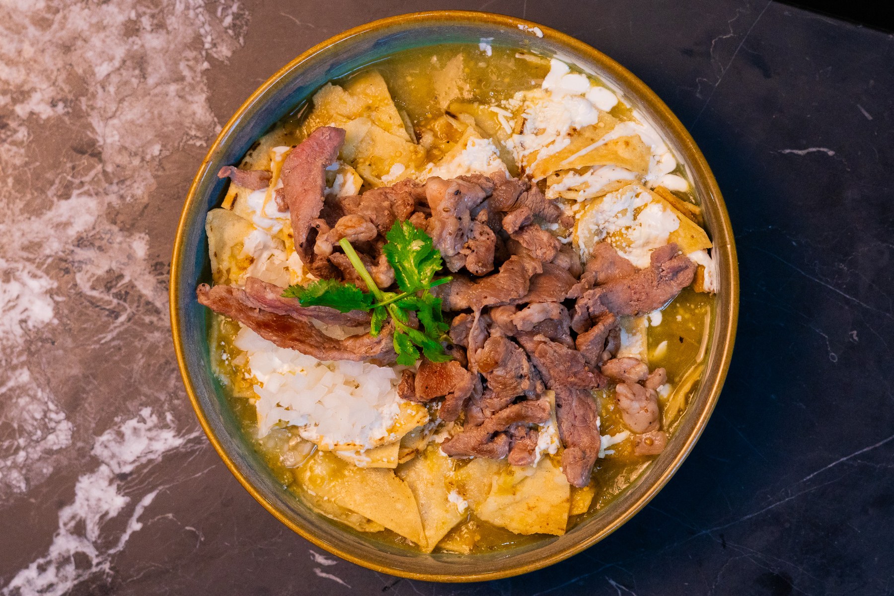 Plato de chilaquiles de Chiflas con salsa, crema y carne, visto desde arriba.