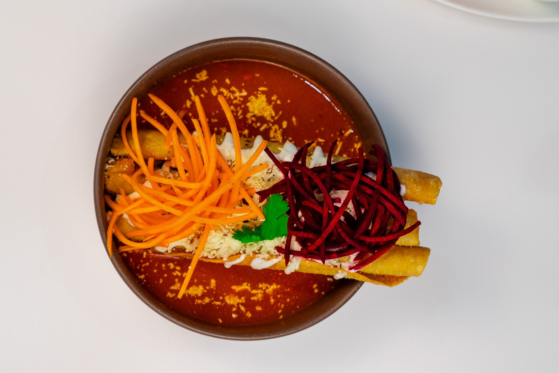 Plato de flautas de Chiflas con crema, queso y guarnición, visto desde arriba.
